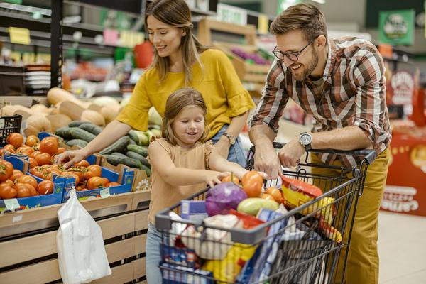 A mother and father in a grocery store with their daughter, all gathered around a cart full of produce.
