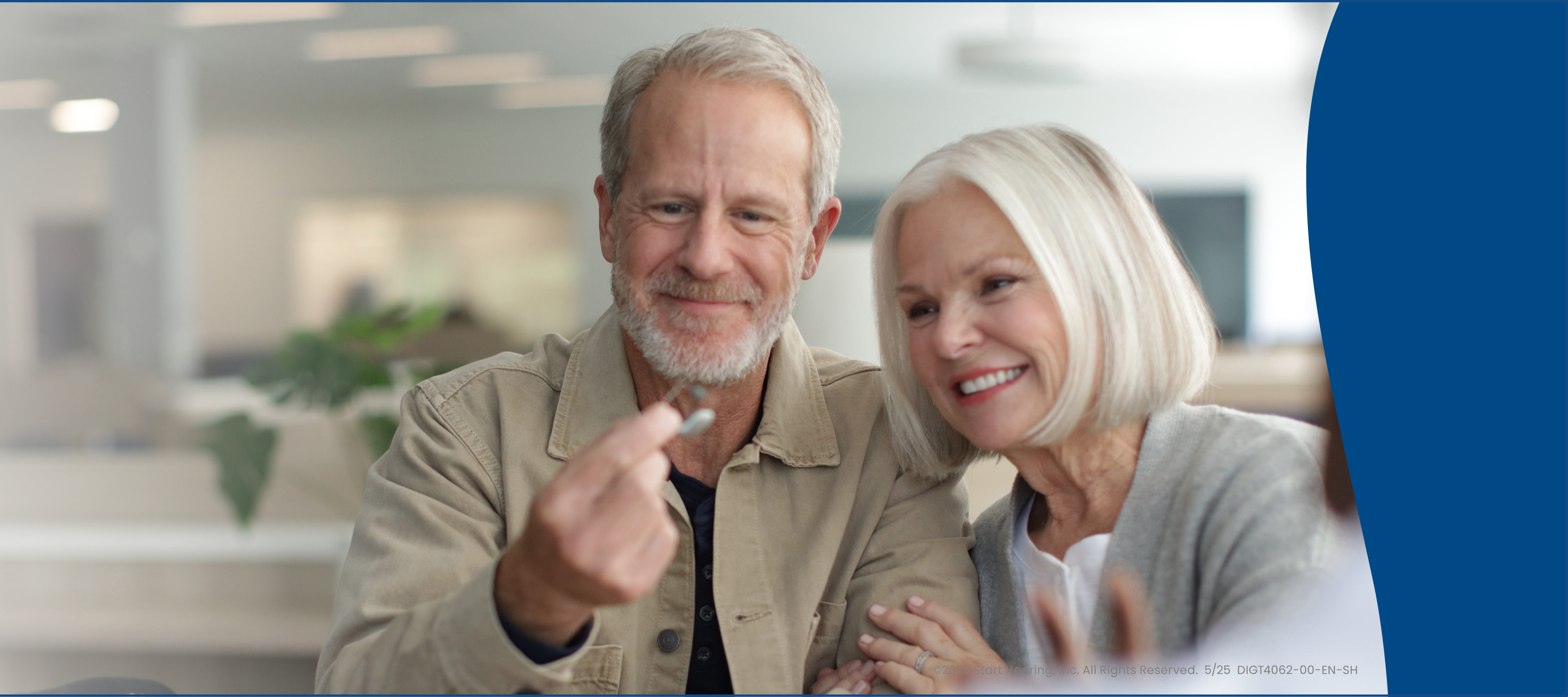 An older couple smiling while looking at hearing aids.