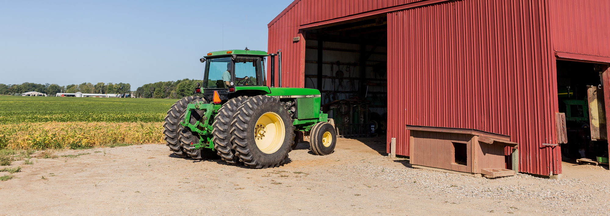 Wide shot of a John Deere tractor parked outside of a large red barn.