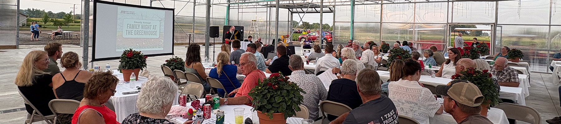 Wide shot of a county annual meeting taking place in a green house.