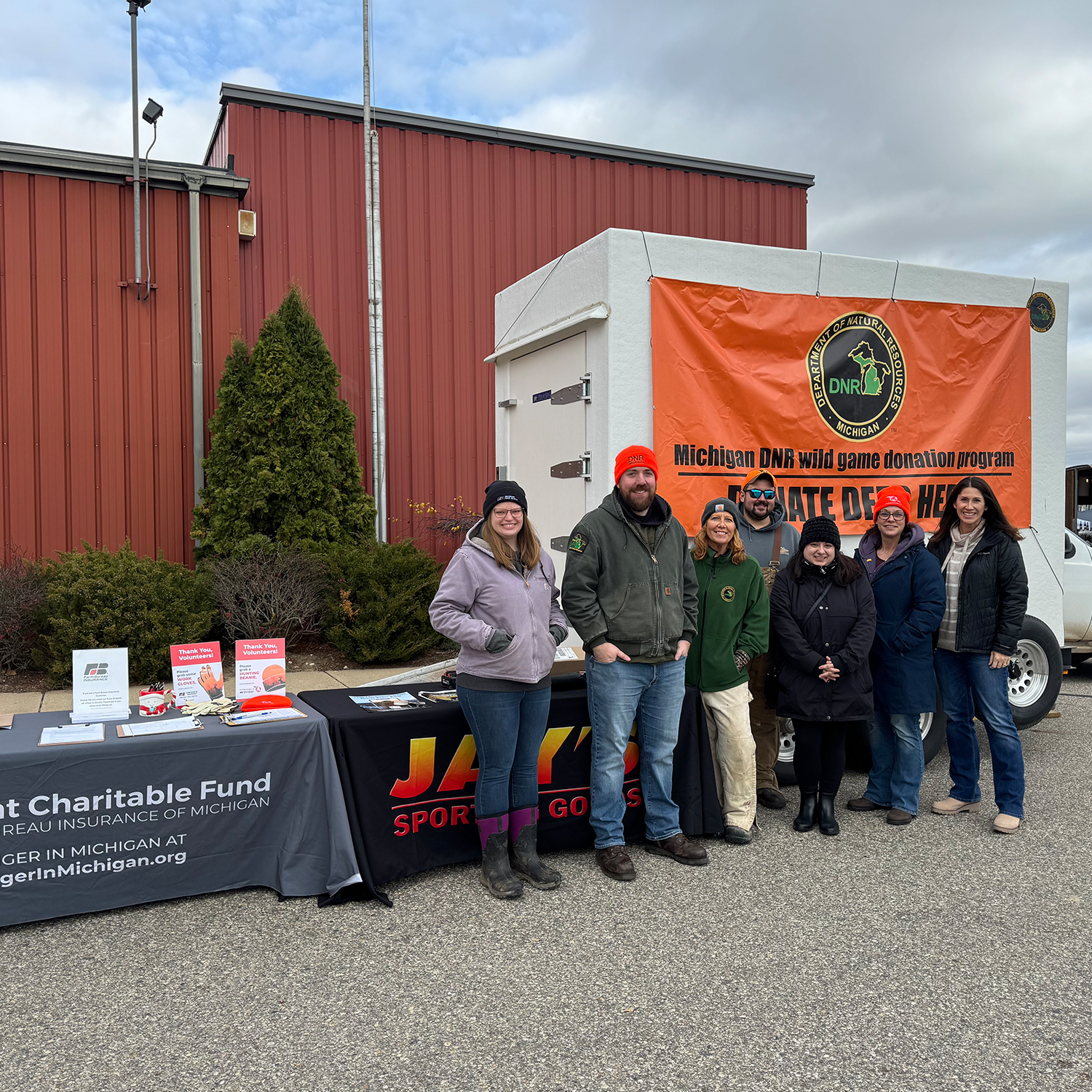 Six people smiling at the camera while standing in front of a deer donation trailer.