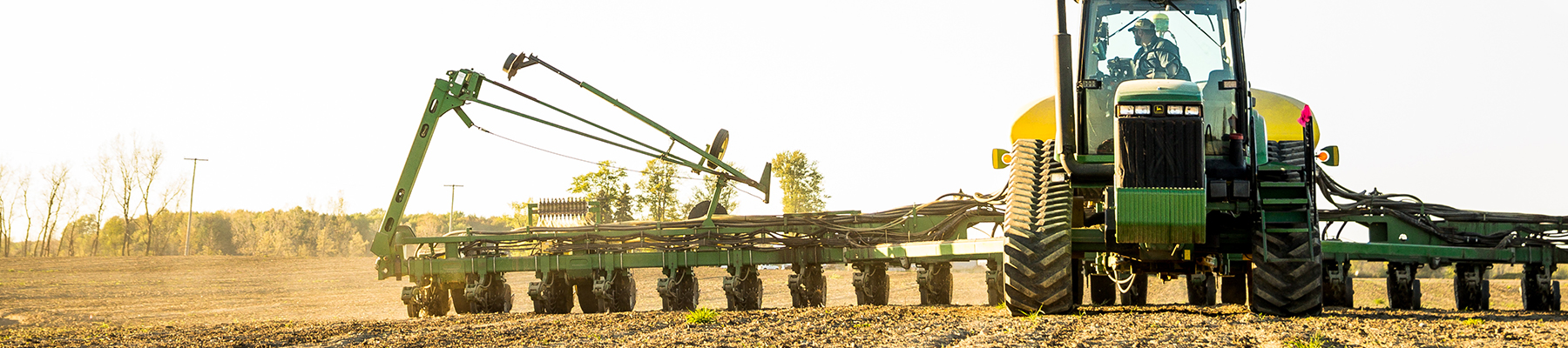 Head-on shot of a John Deere tractor operating in a field at sunset.