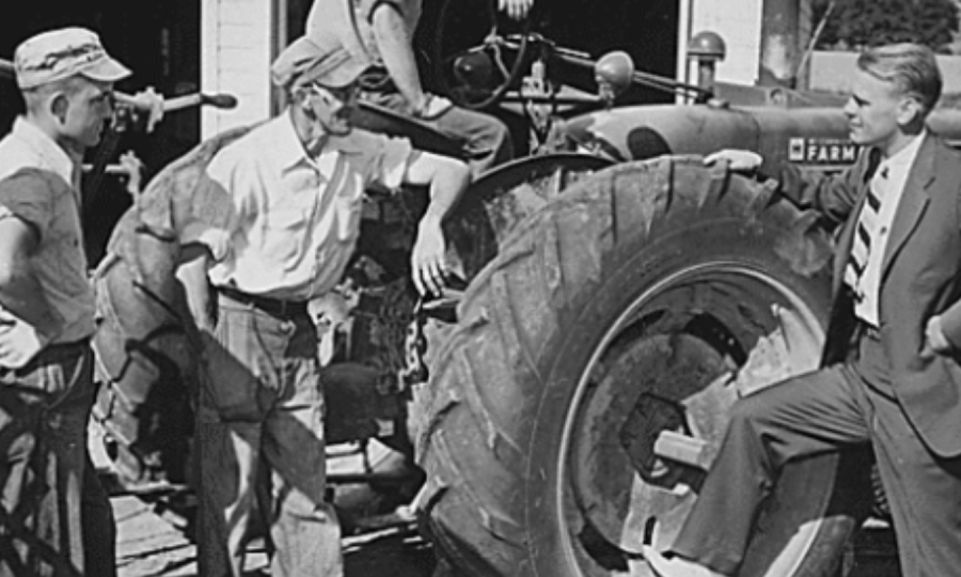 Gerald Ford makes a campaign stop at a farm in Kent County, Michigan 1948. He has his foot on the back tire of a tractor while talking with 3 farmers.