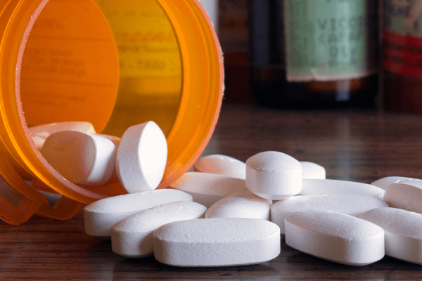 An orange pill bottle on its side with white pills spilling out of it.