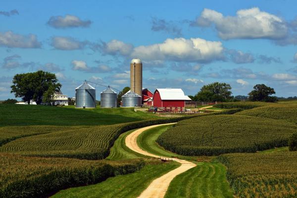 a long winding drive that leads to a farm with a red barn and silos.