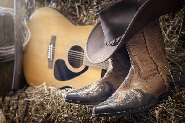 Cowboy boots, hat, and acoustic guitar arranged on a hay bale.