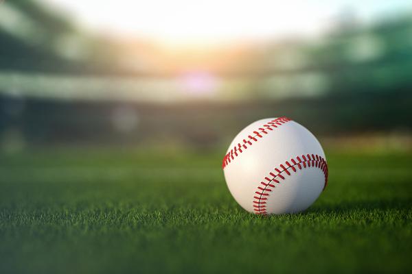 A single baseball resting on the field of a baseball stadium.