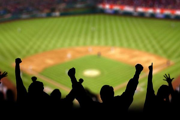 Silhouette of a group of people cheering in front of a baseball diamond.