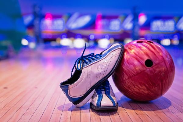 A bowling ball and bowling shoes arranged at the front of a bowling lane under neon lighting.