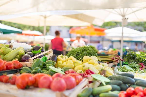 A table full of fresh vegetables set up at a tent in a farmers market.