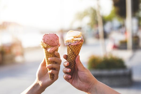 Two different hands holding up ice cream cones to the camera.