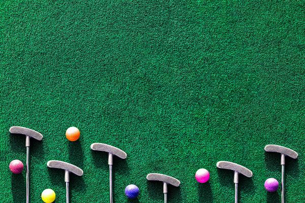 Top-down view of putters and colorful golf balls arranged on a putting green.