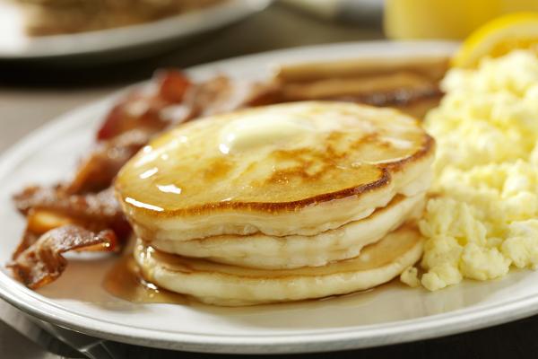 Close-up of a plate loaded with pancakes, scrambled eggs, and bacon.