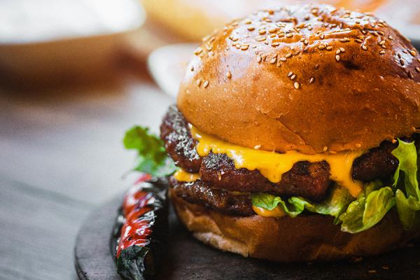Double cheeseburger with french fries and vegetables on wooden cutting board