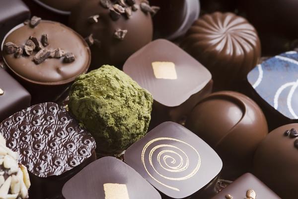 Assorted handmade chocolates in a row. Dark brown with golden ornaments.