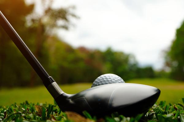 Close-up of a driver behind a teed-up golf ball on a golf course.