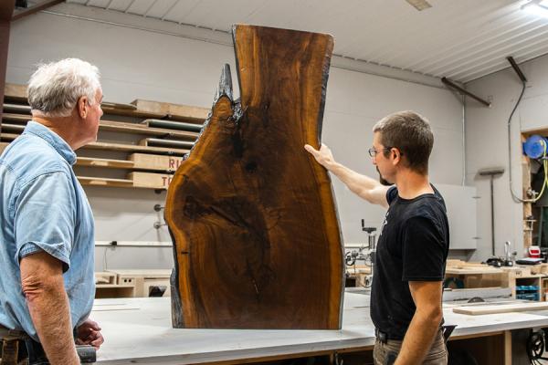 A carpenter showing a large stained piece of a hardwood with natural edges to a customer.
