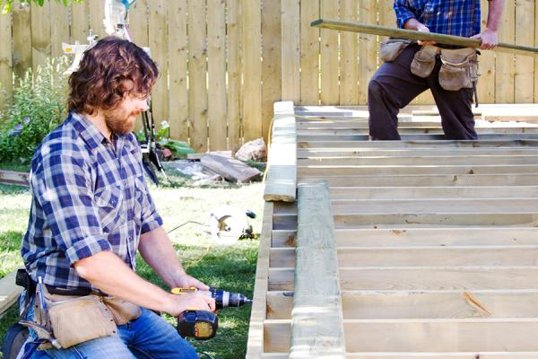 Two men building a deck in the back yard of a home.
