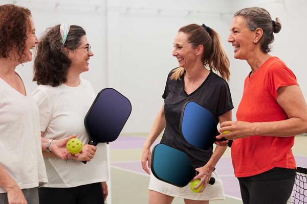Four middle-aged women in sports attire standing next to the net on a pickleball court.