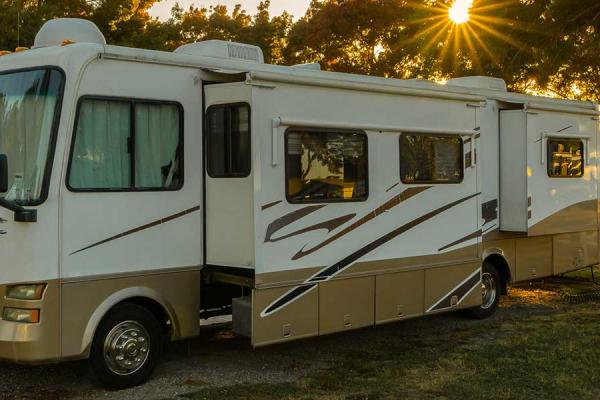 Wide shot of an RV parked at a campground with the sun rising in the background.
