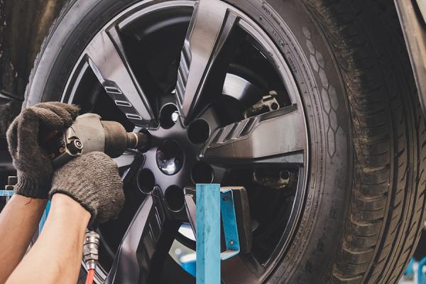 A car mechanic changing the tire of a car on a lift.