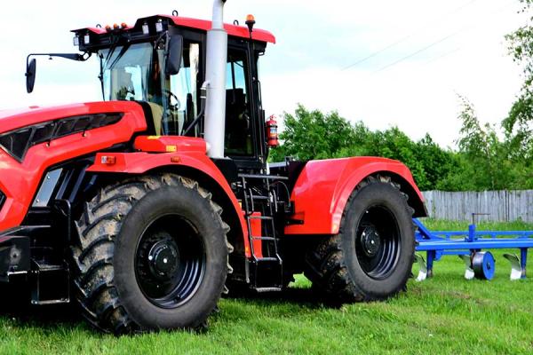 A red tractor is on a grassy field with a blue plow in the background