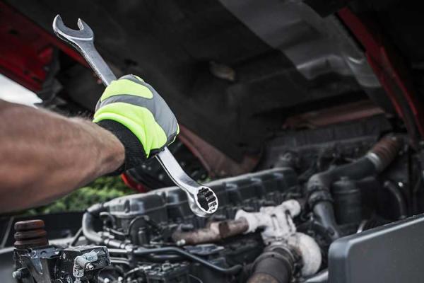 A mechanic using a wrench to work under the hood of a semi-truck.