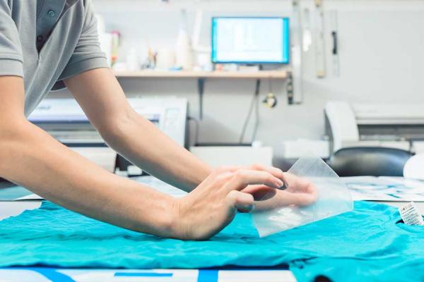 Woman printing a T-shirt as promotional item in workshop.