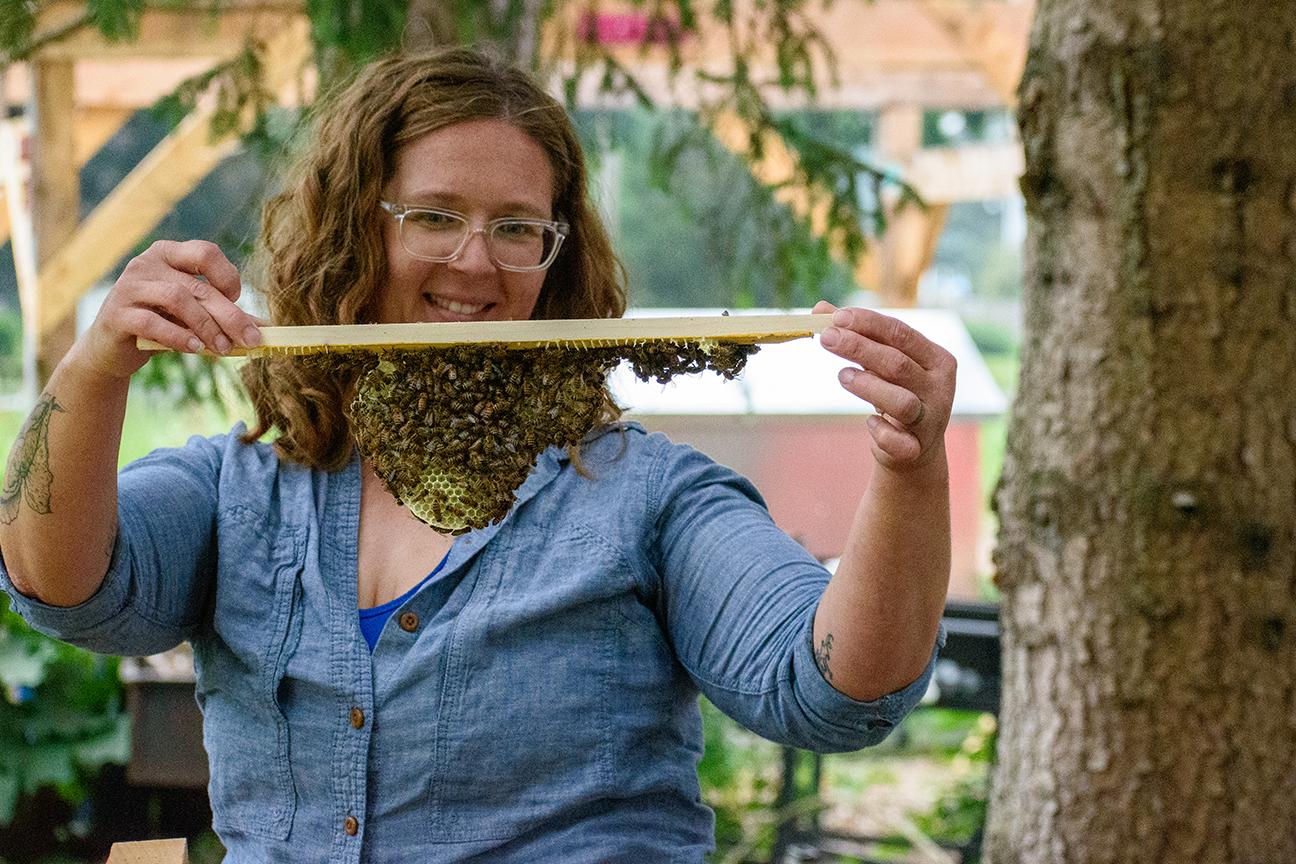A woman holding up a honeybee hive to her face to examine it.