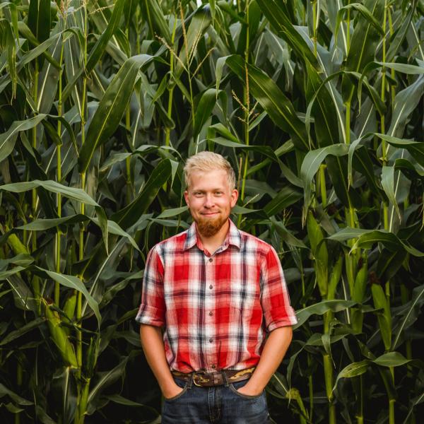 Young farmer stands in front of tall corn