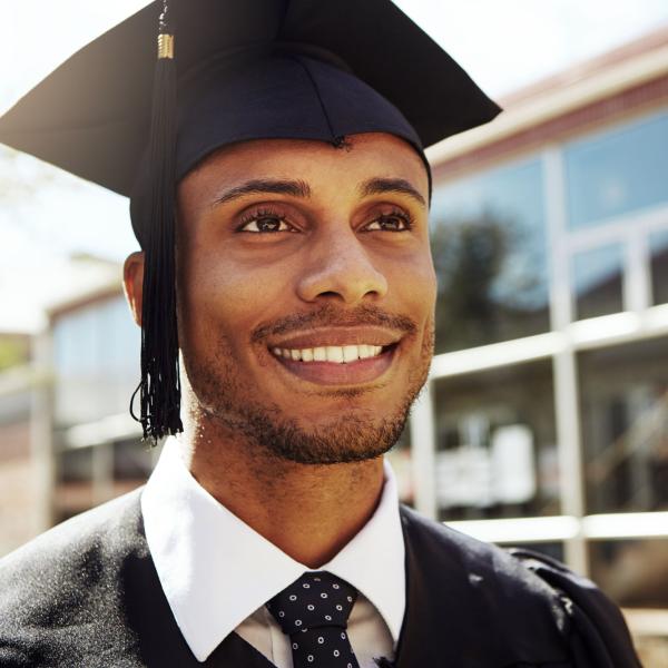 Man in graduation cap and gown happily looks off into the distance