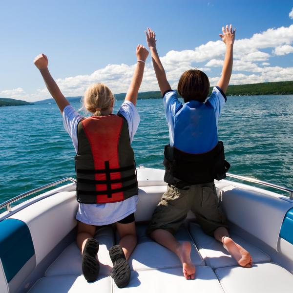 Two kids sit at the front of a boat with their arms in the air