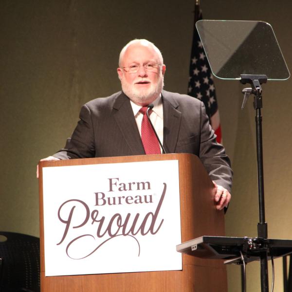 A man talks behind a podium that says "farm bureau proud"
