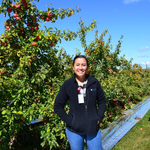 woman stands by apple tree's and smiles at the camera