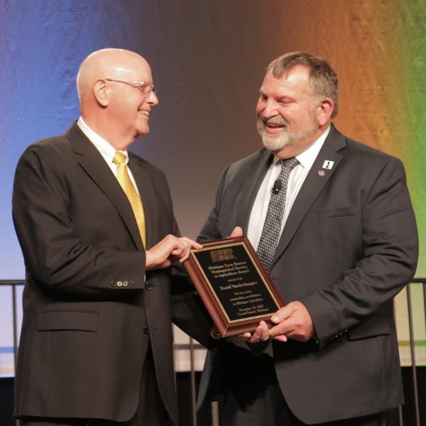 MFB president Carl Bednarski presenting David VanderHaagen with a DSA award plaque on stage at the MFB 2022 State Annual Meeting.