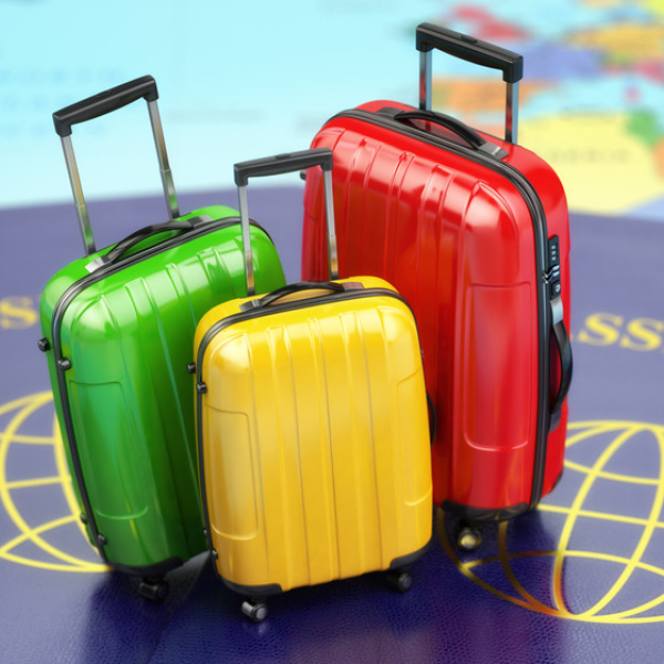 Stylized shot of a three rolling suitcases — one green, one red, and one yellow — sitting atop a pair of oversized passports.