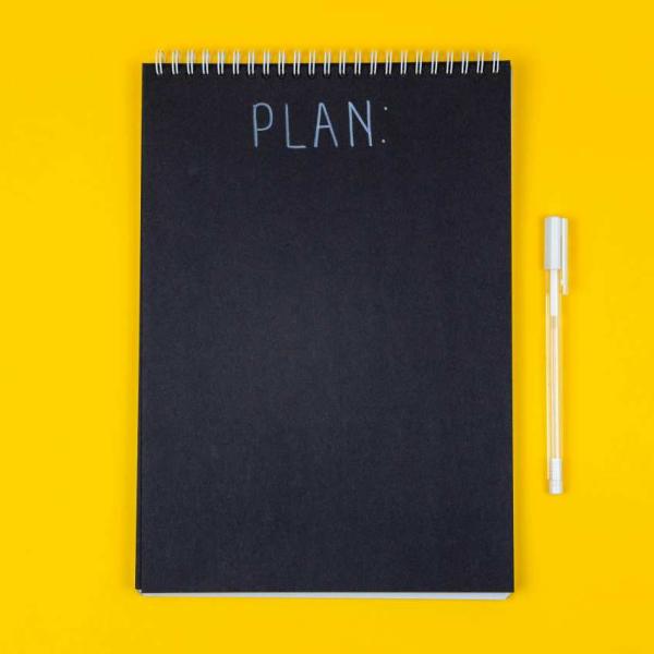 A black notebook titled PLAN rests on a yellow background.