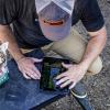 A farmer kneeling at a bench to use a tablet computer.