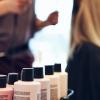 Close-up of hair products in foreground with out of focus stylist and client in background.