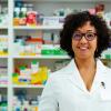 A pharmacist smiling at the camera while standing behind the counter of a pharmacy.