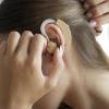 Profile view of a woman putting a hearing aid into her ear.